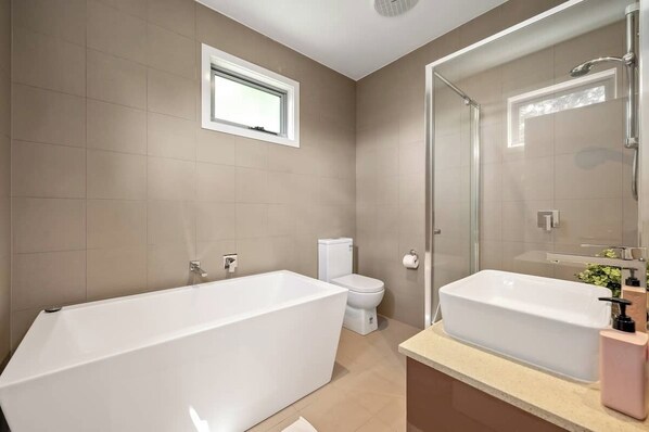 A modern bathroom with a bathtub, a toilet, a shower, and a sink. - Relaxing Getaway Oasis with Patio in Charming Kew (Kew)