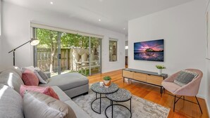 A modern living room with a sofa, coffee table, and armchair, a painting on the wall, and a sliding glass door leading to an outdoor area.
