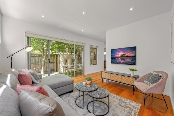 Un salon moderne avec un canapé, une table basse et un fauteuil, un tableau accroché au mur et une porte-fenêtre coulissante donnant sur un espace extérieur.