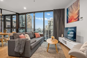 A modern living room with a sofa, coffee table, TV, and large windows with a city view. - North Facing Skyline Views near Crown & Yarra River (Southbank)