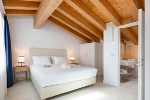 Quarto com cama, mesas de cabeceira, guarda-roupa e porta aberta para um banheiro.