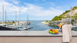 Ein Yachthafen mit vertäuten Booten, Blick auf das Meer und eine Obstschale auf einem Balkon.