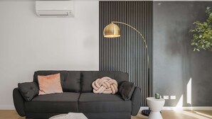 A modern living room with a black sofa, a gold floor lamp, a textured wall, and a small white table with a plant. - Executive Designer Dreaming Home with All you need (Moonee Ponds)