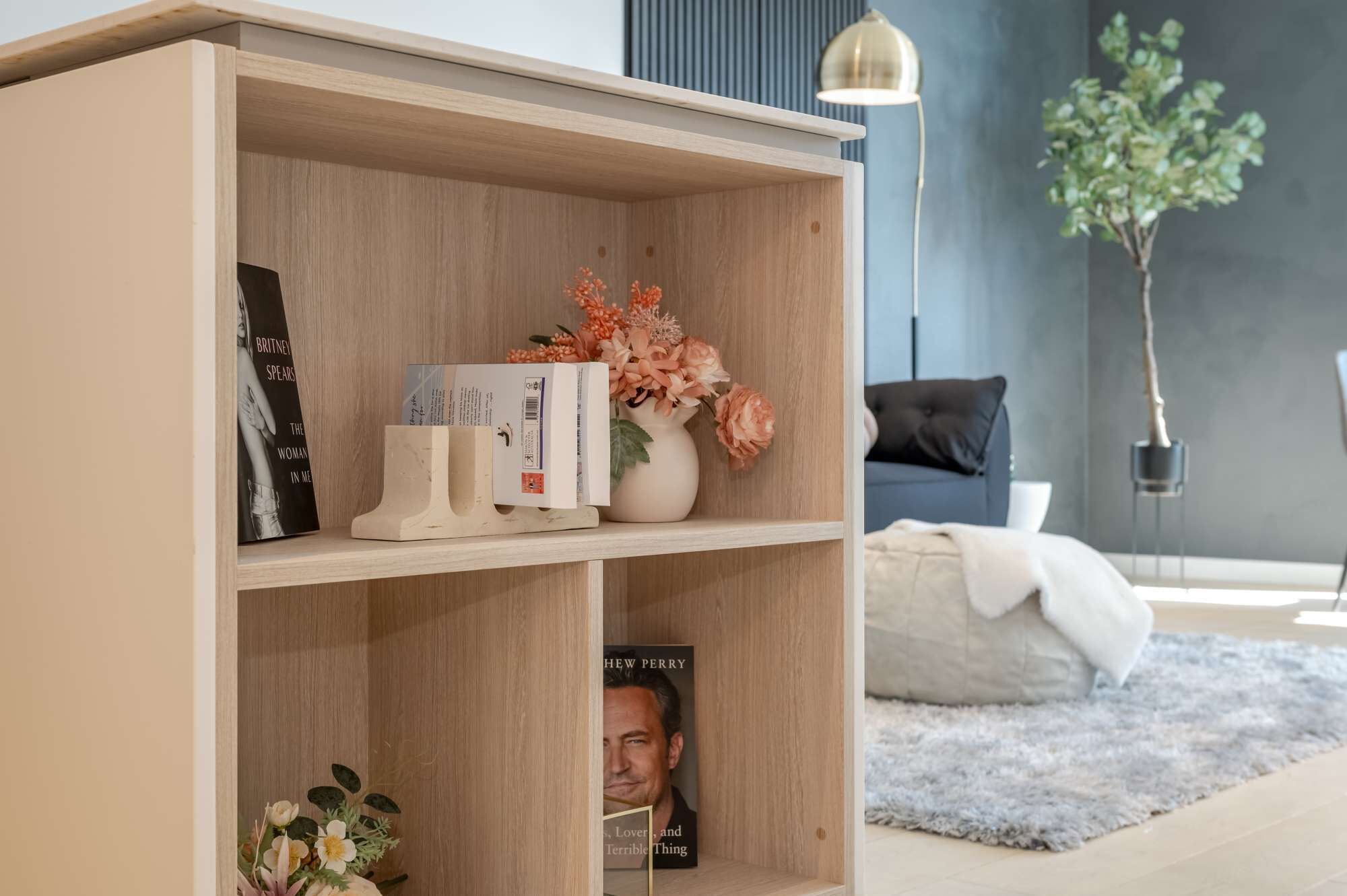 Ein Bücherregal mit Büchern und Dekoration, ein Sofa, eine Lampe und eine Pflanze in einem modernen Wohnzimmer.