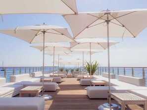 A deck with white lounge chairs and umbrellas, overlooking the sea.