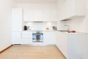 Una cocina moderna con armarios blancos, horno de acero inoxidable, cafetera y un lavamanos.