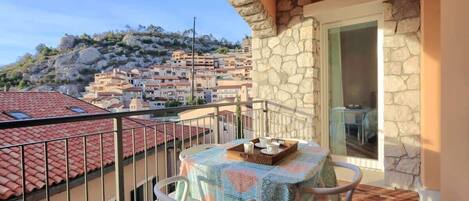 A balcony with a table and chairs, overlooking a town with red-roofed buildings.