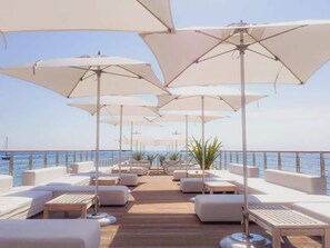 A deck with white outdoor seating and umbrellas, overlooking the sea.