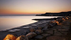 Ett hotell vid stranden med en stenlagd gångväg som leder ner till havet, utrustat med solstolar och en stenstrand.