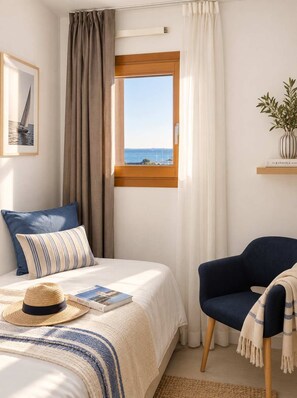 Ein Schlafzimmer mit einem Bett, einem Sessel, einem Fenster mit Meerblick, einem gerahmten Bild an der Wand und einer Pflanze auf einem Regal.