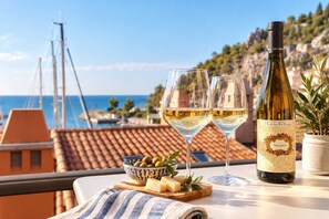A table with a bottle of wine, two glasses, a bowl of olives, and a potted plant.