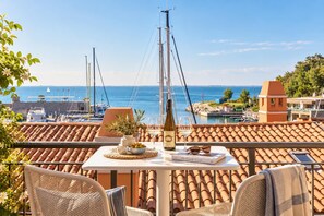 A terrace with a table set for dining, overlooking a marina with boats and a clear view of the sea.