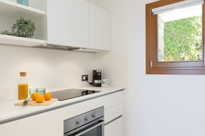 Une cuisine moderne avec des meubles blancs, un four encastré, une machine à café et une fenêtre donnant sur un paysage verdoyant.