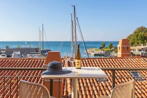 Eine Terrasse mit Tisch, Stühlen und einer Weinflasche mit Blick auf einen Yachthafen, Boote und einen klaren Himmel.