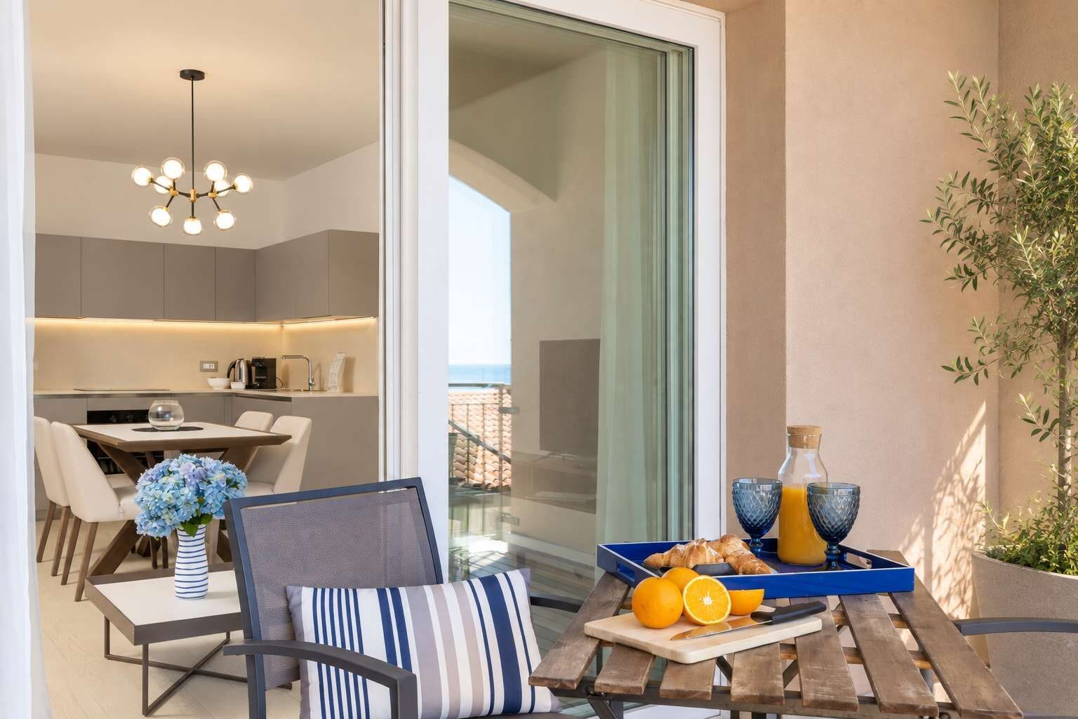 A modern dining area with a table set for two, a blue vase with flowers, and a tray with croissants and orange juice.
