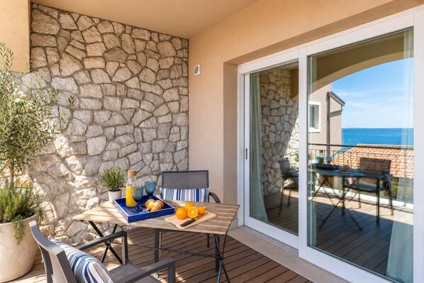 Un balcón con un muro de piedra, una mesa con alimentos para el desayuno y vista al mar.