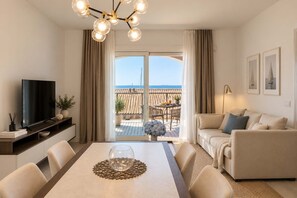 Un salon moderne doté d’un téléviseur à écran plat, d’une table à manger agrémentée d’un élément décoratif, d’un canapé et d’un balcon offrant une vue sur la mer.