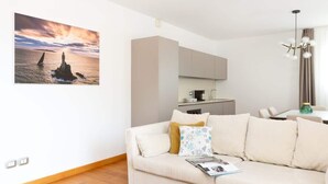 Ein Wohnzimmer mit einer Couch, einer Zeitschrift, einem Gemälde eines Leuchtturms und einer Küche im Hintergrund.