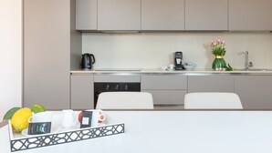 Eine moderne Küche mit Kaffeemaschine, Wasserkocher und einem Blumenstrauß. Zwei weiße Stühle und ein Esstisch mit einer Auswahl an Frühstücksartikeln.