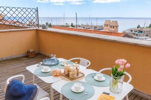A balcony with a table set for two, a vase of pink tulips, and a view of the sea.