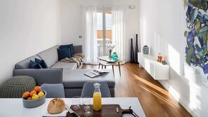 A modern living room with a sofa, dining table, and a view of the balcony.