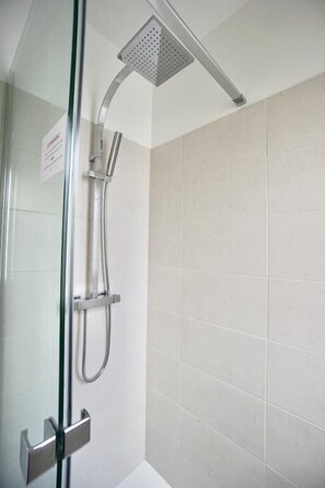 A glass-enclosed shower area with a handheld showerhead and a fixed overhead showerhead.