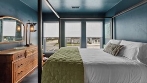 A bedroom with a large bed, a dresser, and a mirror. There are windows with blinds, and a view of the outside. - Downtown, Uniquely Designed, Near the Beach (Sheboygan)