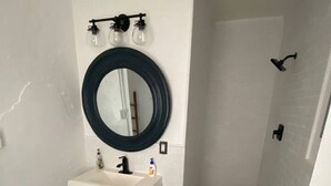 A bathroom with a white sink, a round mirror, a shower, and a toilet. - A perfect place in a perfect location (New Orleans)