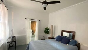 A bedroom with a bed, a ceiling fan, a bedside table, a lamp, and a view of a bathroom. - A perfect place in a perfect location (New Orleans)