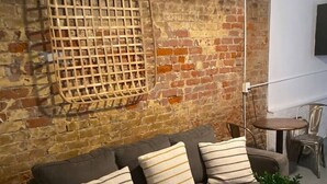 A living room with a brick wall, a sofa with striped cushions, a wooden coffee table, and a small round table with chairs. - A perfect place in a perfect location (New Orleans)