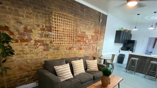 A living room with a brick wall, a grey sofa with striped cushions, a wooden coffee table, and a potted plant. - A perfect place in a perfect location (New Orleans)