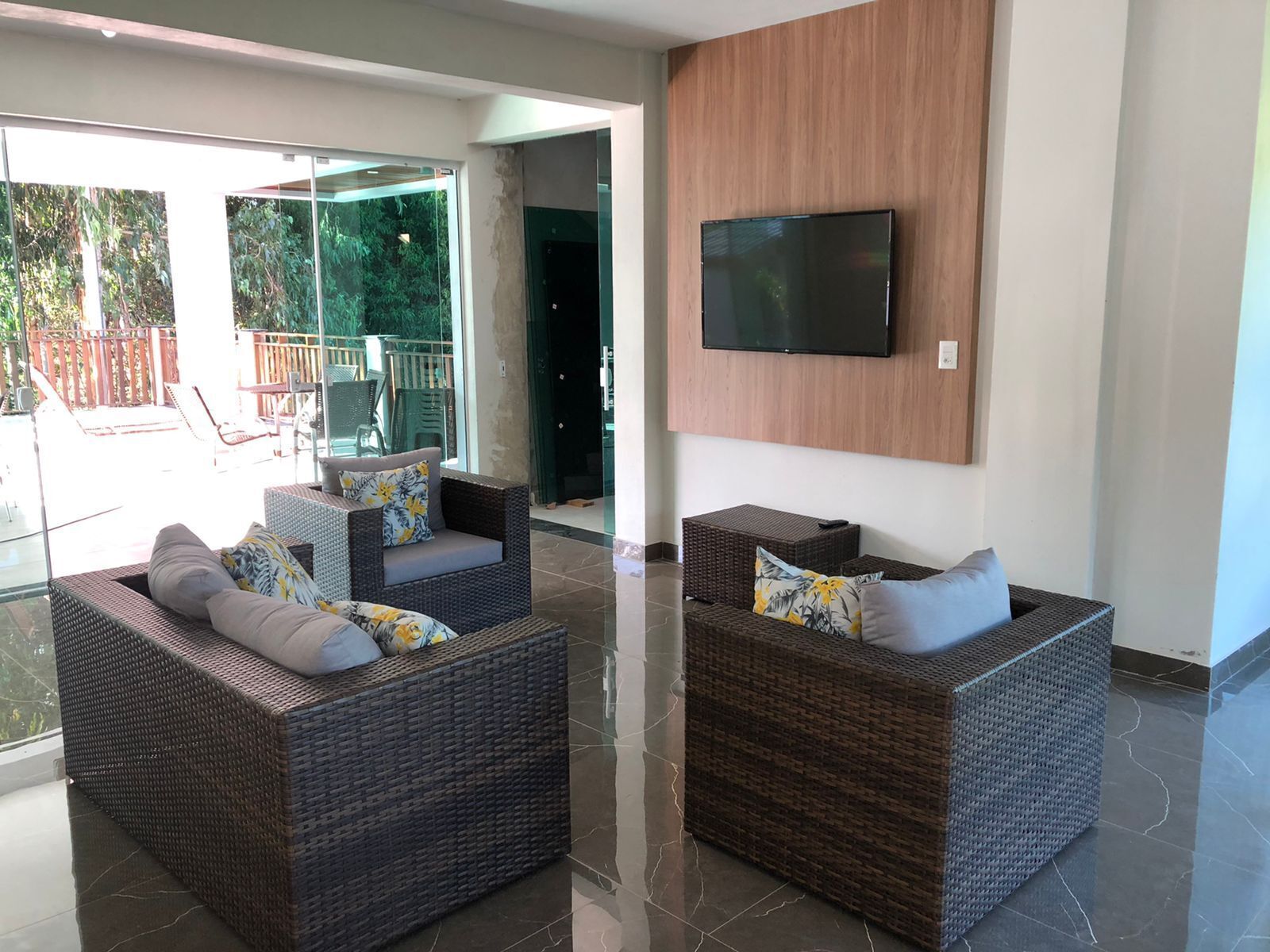 A modern living room with wicker furniture and a flat-screen TV mounted on the wall.