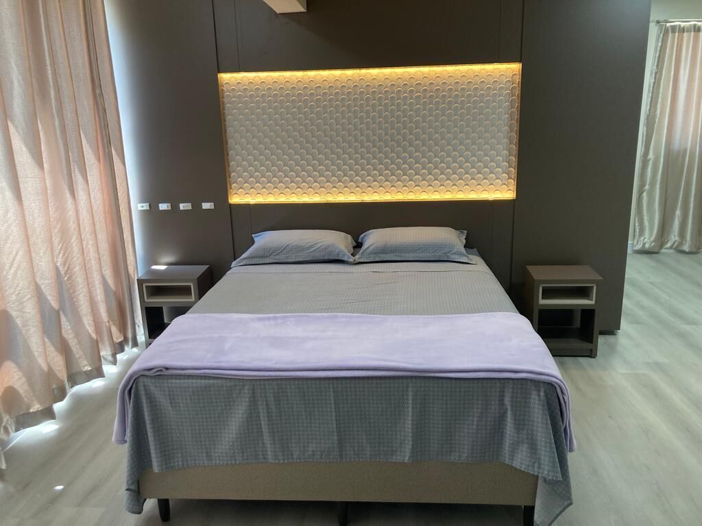 Een moderne slaapkamer met een groot bed, een hoofdbord met een structuurpaneel en nachtkastjes.