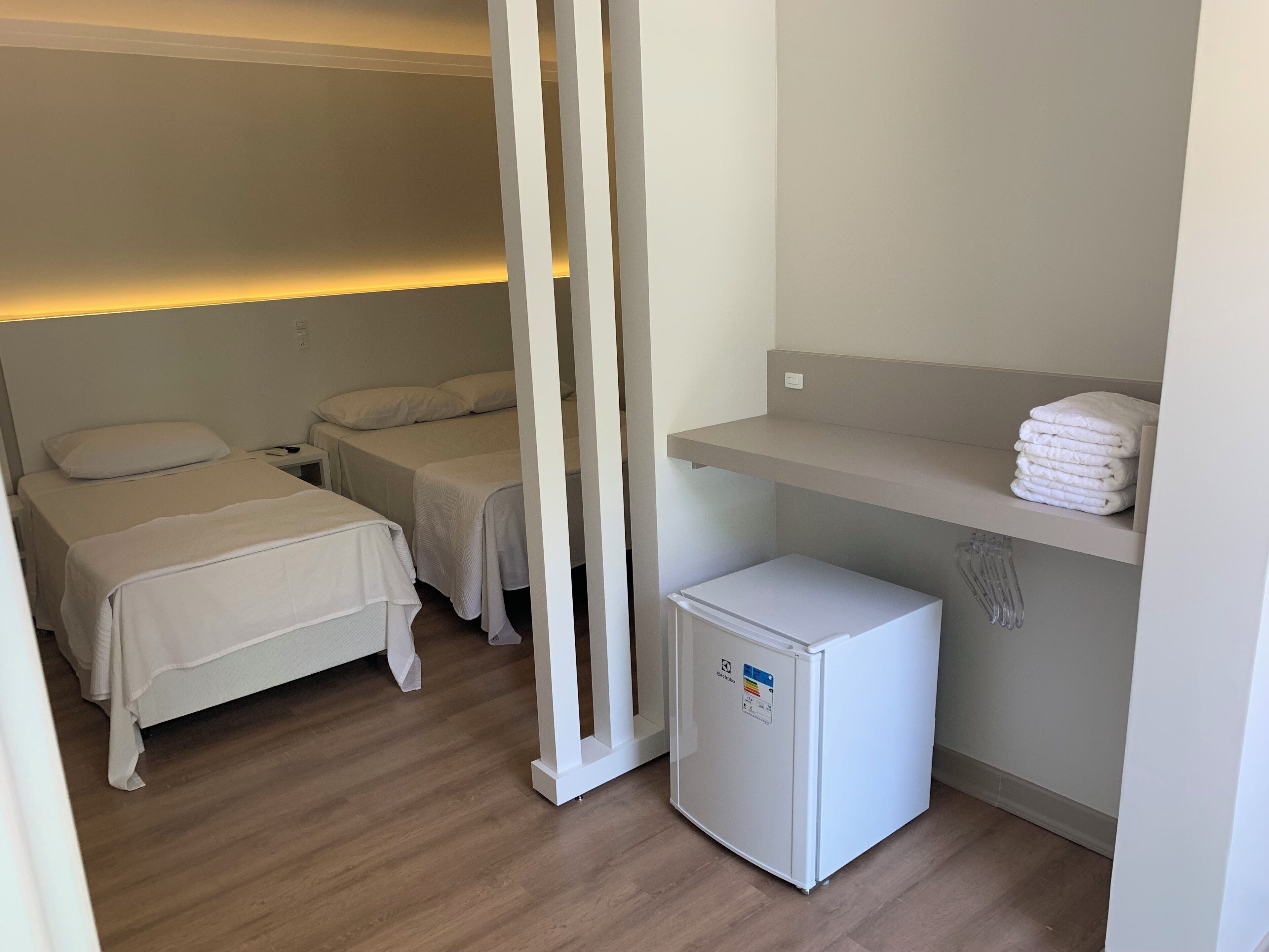 A hotel room with two beds, a small refrigerator, and a shelf with folded towels.