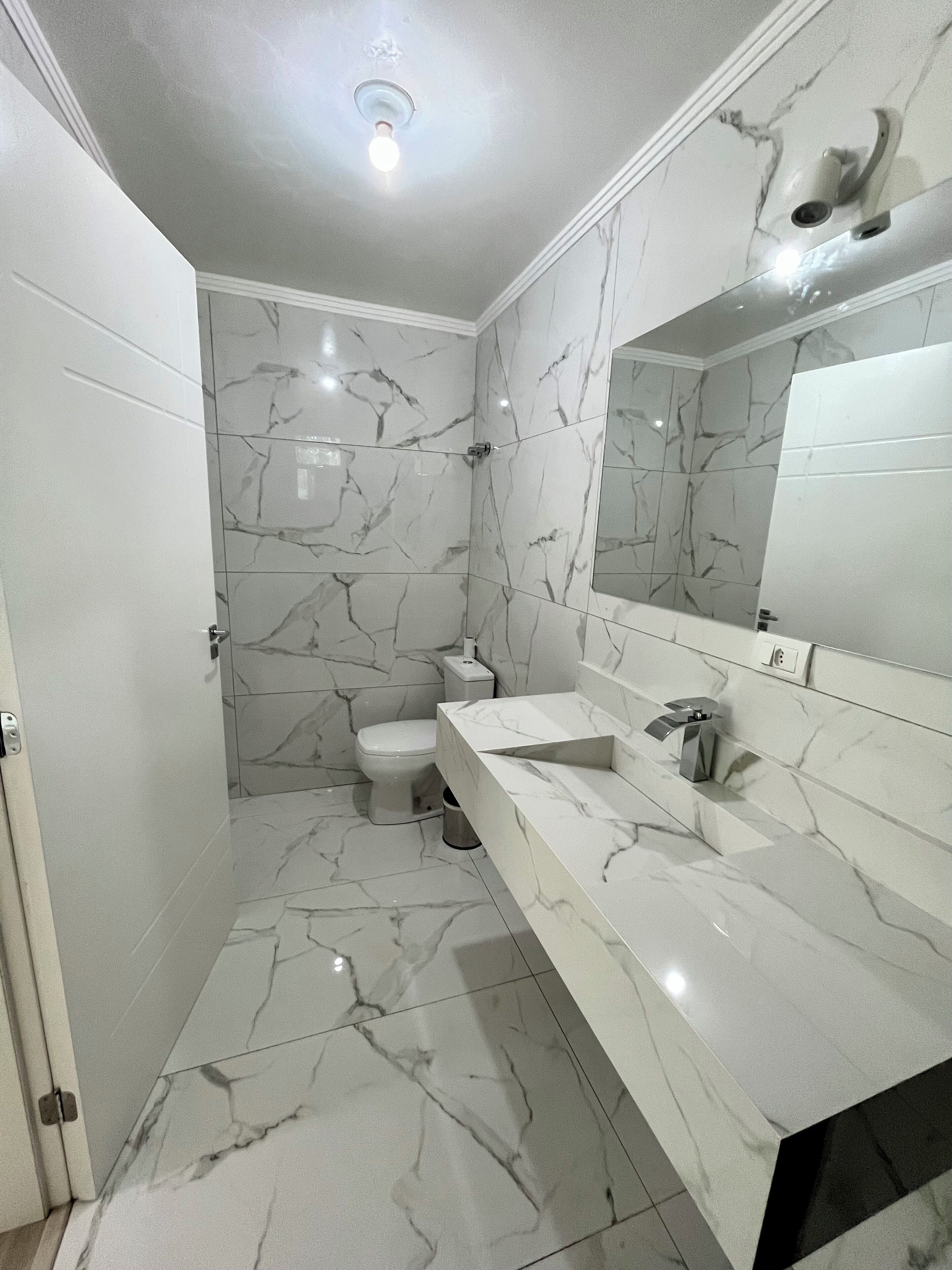 Un baño con suelo de mármol blanco, inodoro blanco, lavabo blanco y un espejo grande.