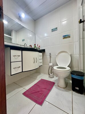 A bathroom with a toilet, a sink with a mirror, and a trash bin.