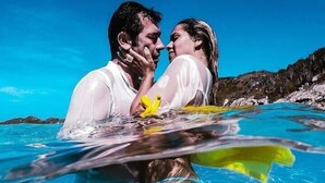 Um casal em uma piscina azul cristalina, com uma paisagem rochosa ao fundo.