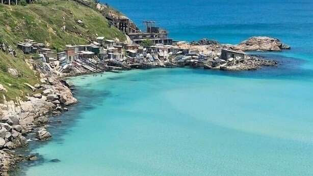 Uma área costeira com águas turquesa cristalinas, costas rochosas e uma pequena praia.