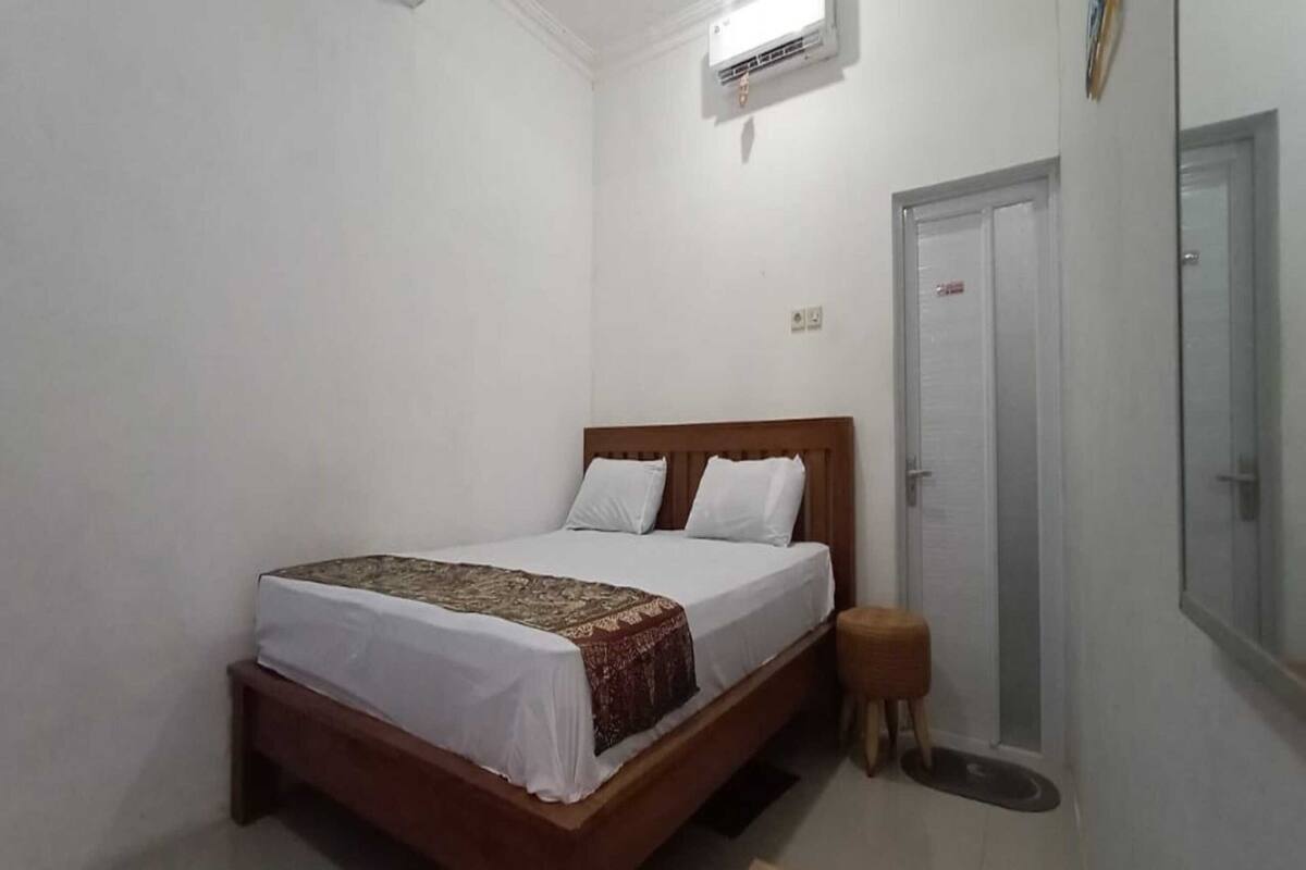 A bedroom with a wooden bed, white bedding, a small stool, and a door with a mirror.