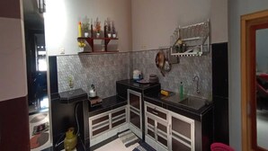 A compact kitchen with black countertops, white cabinets, and a tiled backsplash. There are shelves with decorative items and a sink with a faucet. - Hotel O Homestay Kita Purworejo (Purworejo)