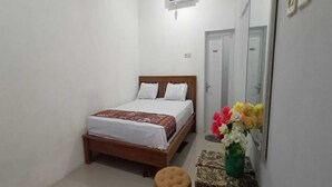 A bedroom with a wooden bed, white bedding, a small stool, a mirror, and a vase with flowers. - Hotel O Homestay Kita Purworejo (Purworejo)
