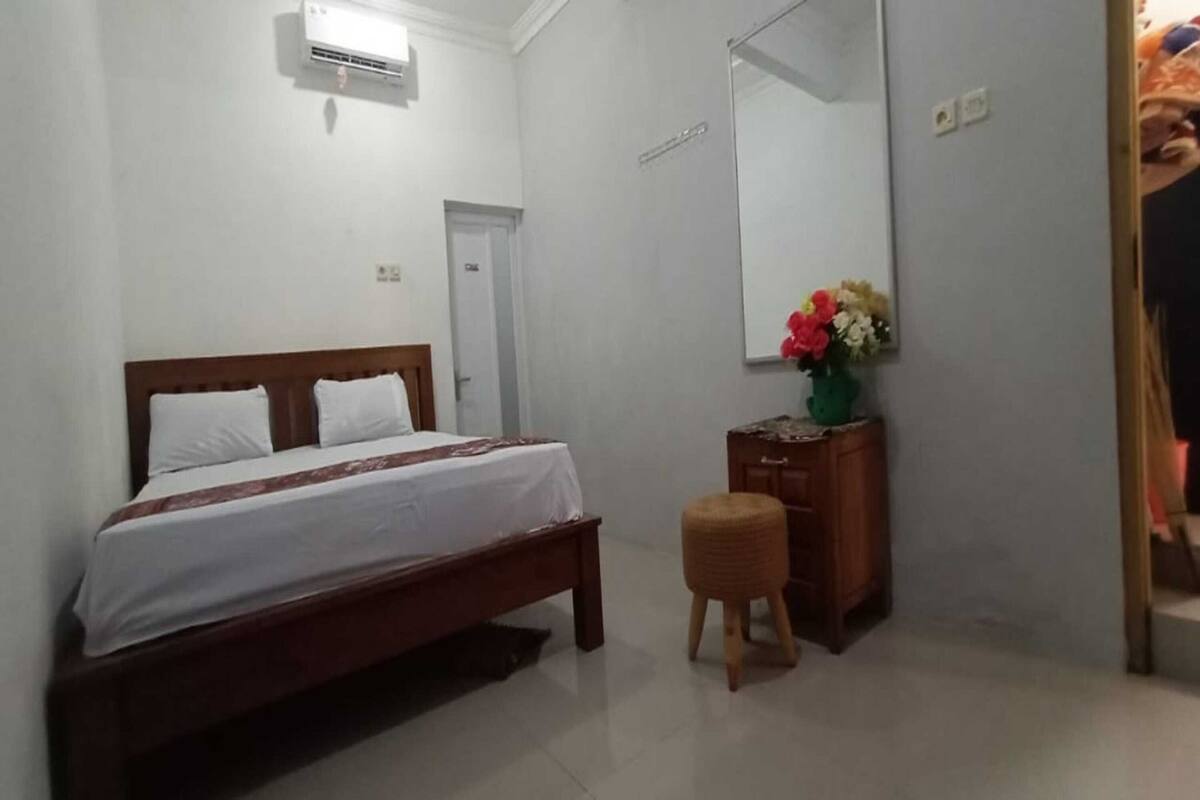 A bedroom with a bed, a wooden nightstand, a mirror, and a small stool.