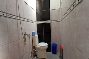 A small bathroom with a toilet, a shower, and a blue trash bin. - Hotel O Homestay Kita Purworejo (Purworejo)