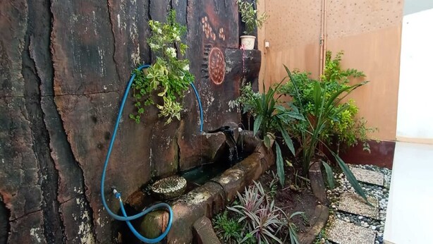 A rustic outdoor area with a wooden wall, a small water feature, and various plants. - Hotel O Homestay Kita Purworejo (Purworejo)