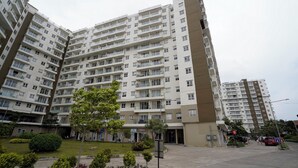 Un edificio residencial de varios pisos con balcones, un patio ajardinado y un área de estacionamiento.