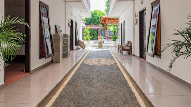 A hallway with a tiled floor, a central rug, and potted plants on either side.