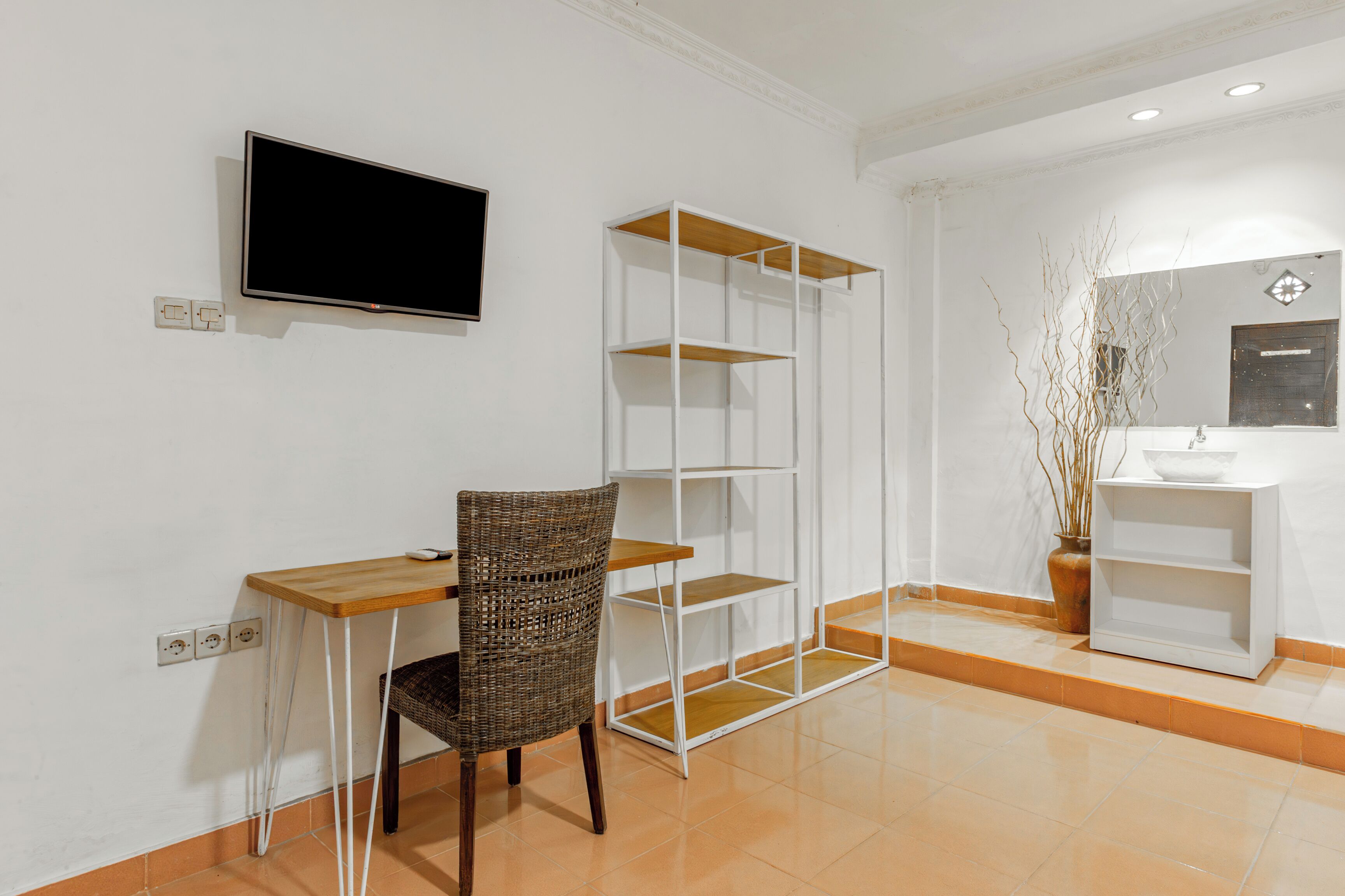 A room with a desk, chair, TV, shelves, and a bathroom with a mirror and sink.