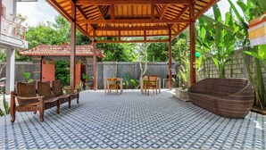 A covered patio with a patterned tile floor, wooden furniture, and a large woven chair.
