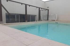 An indoor swimming pool with clear water, surrounded by a tiled deck and a metal frame structure.