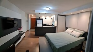 A modern hotel room with a large bed, a TV, a desk, and a kitchenette. - Saint Sebastian ap113-stúdio para casal (Jaragua do Sul)